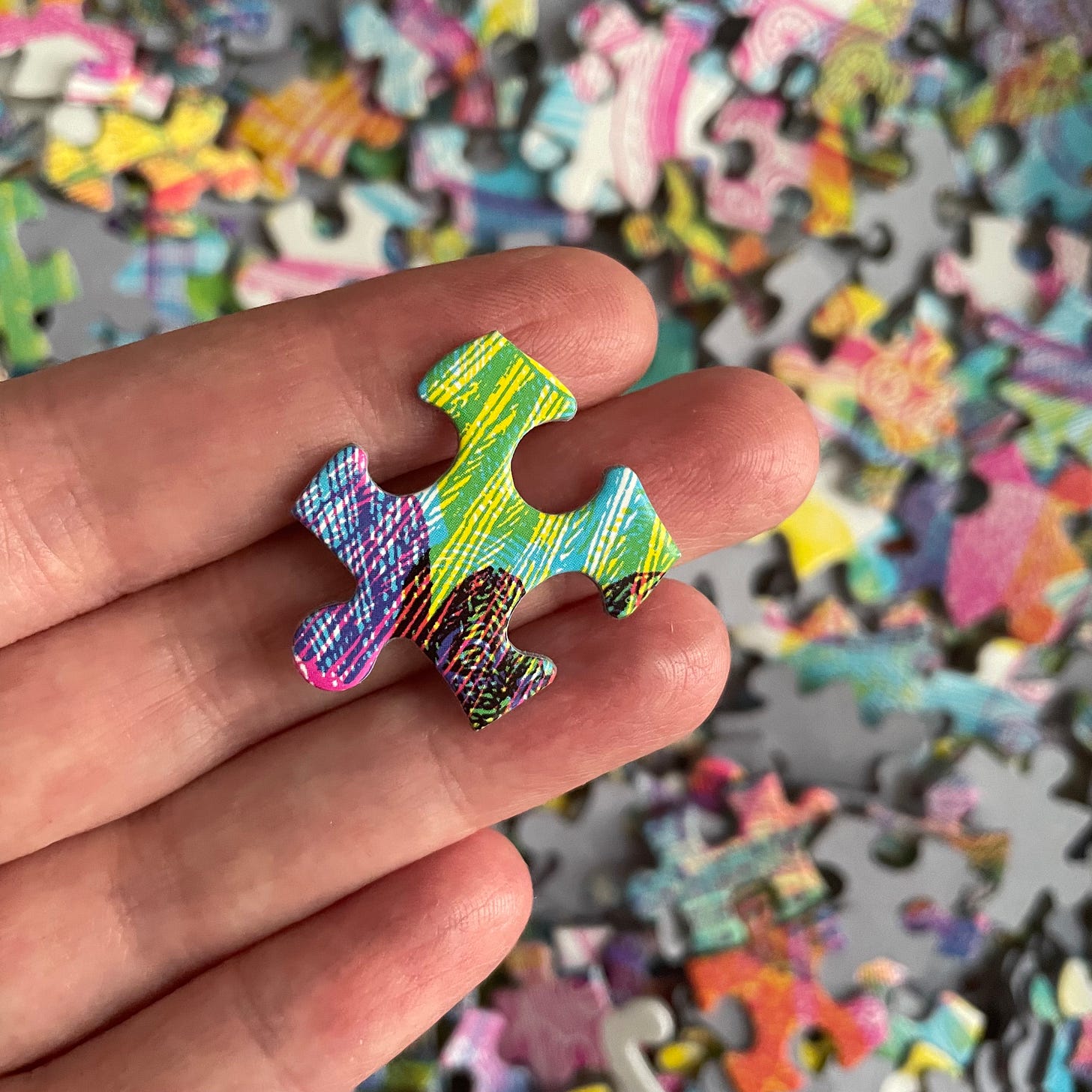 Photo of a colorful jigsaw puzzle piece on a hand, in front of a dense background of many puzzle pieces.