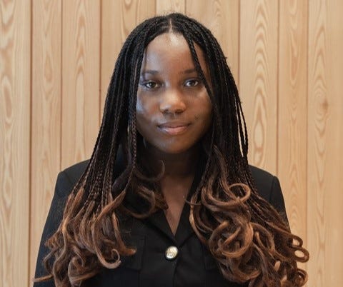 Picture of Zara headshot. She has long brown dreadlocks and is wearing a black suit