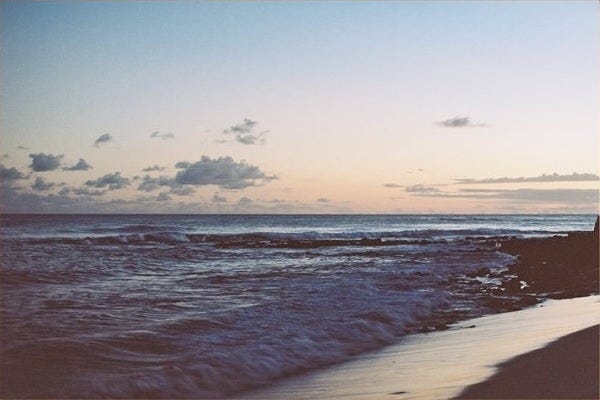 May include: A framed photograph of a beach scene with a blue sky, white clouds, and a calm ocean with waves crashing on the shore. The sand is light brown and the water is a deep blue.