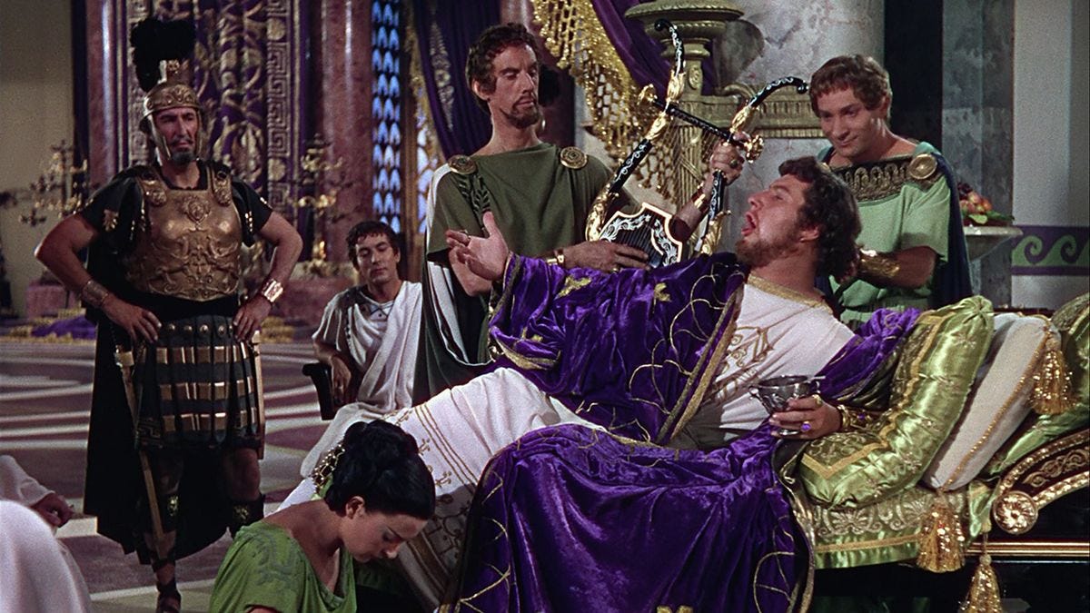 Publicity still from 1951 epic film Quo Vadis - Peter Ustinov as Nero reclines on a couch and declaims to a group of soldiers and servants