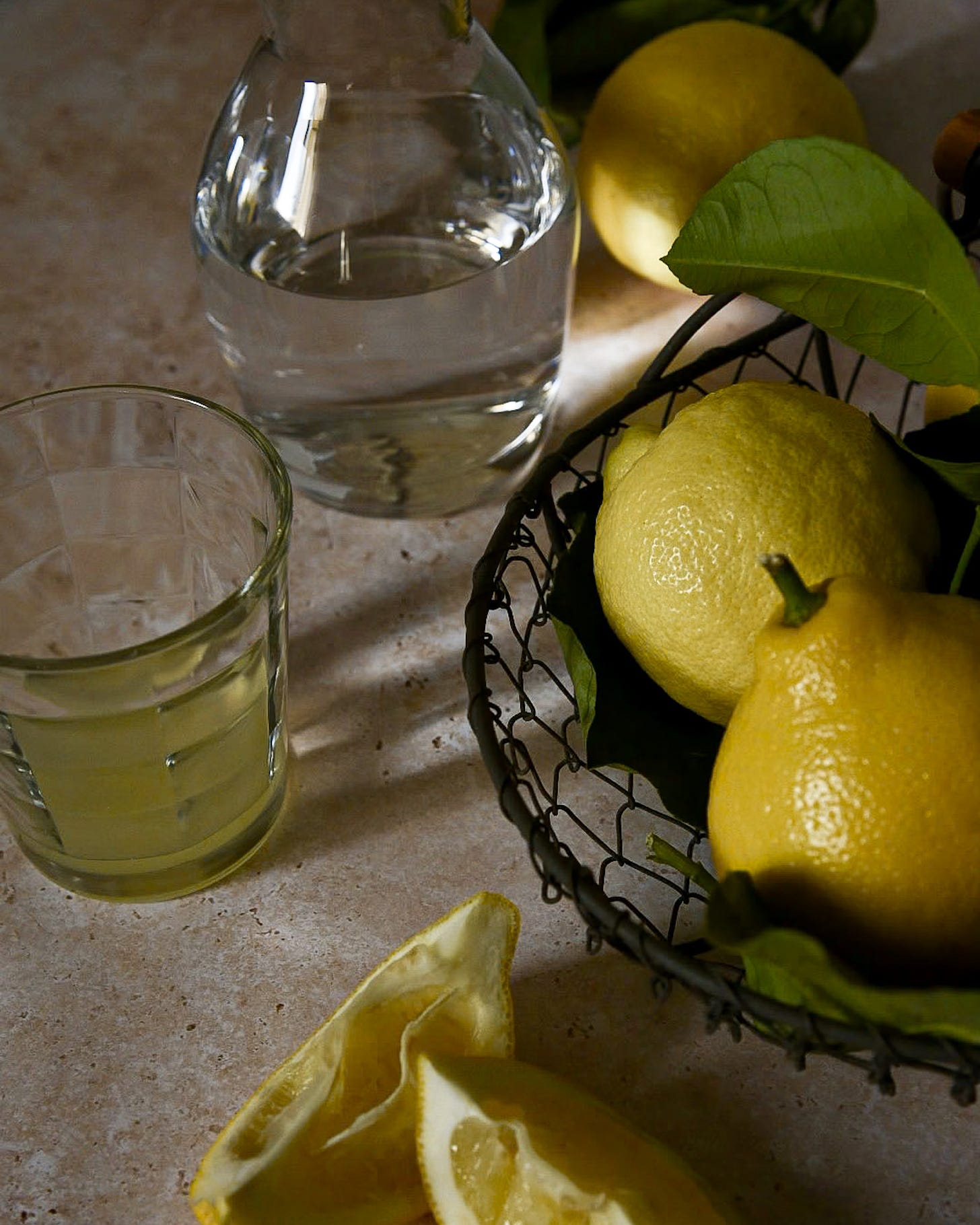 A glass with lemonade, and black wire basket with lemons