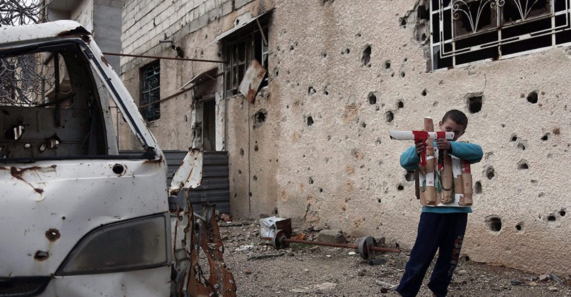 A Syrian child plays with a cardboard gun in Eastern Ghouta