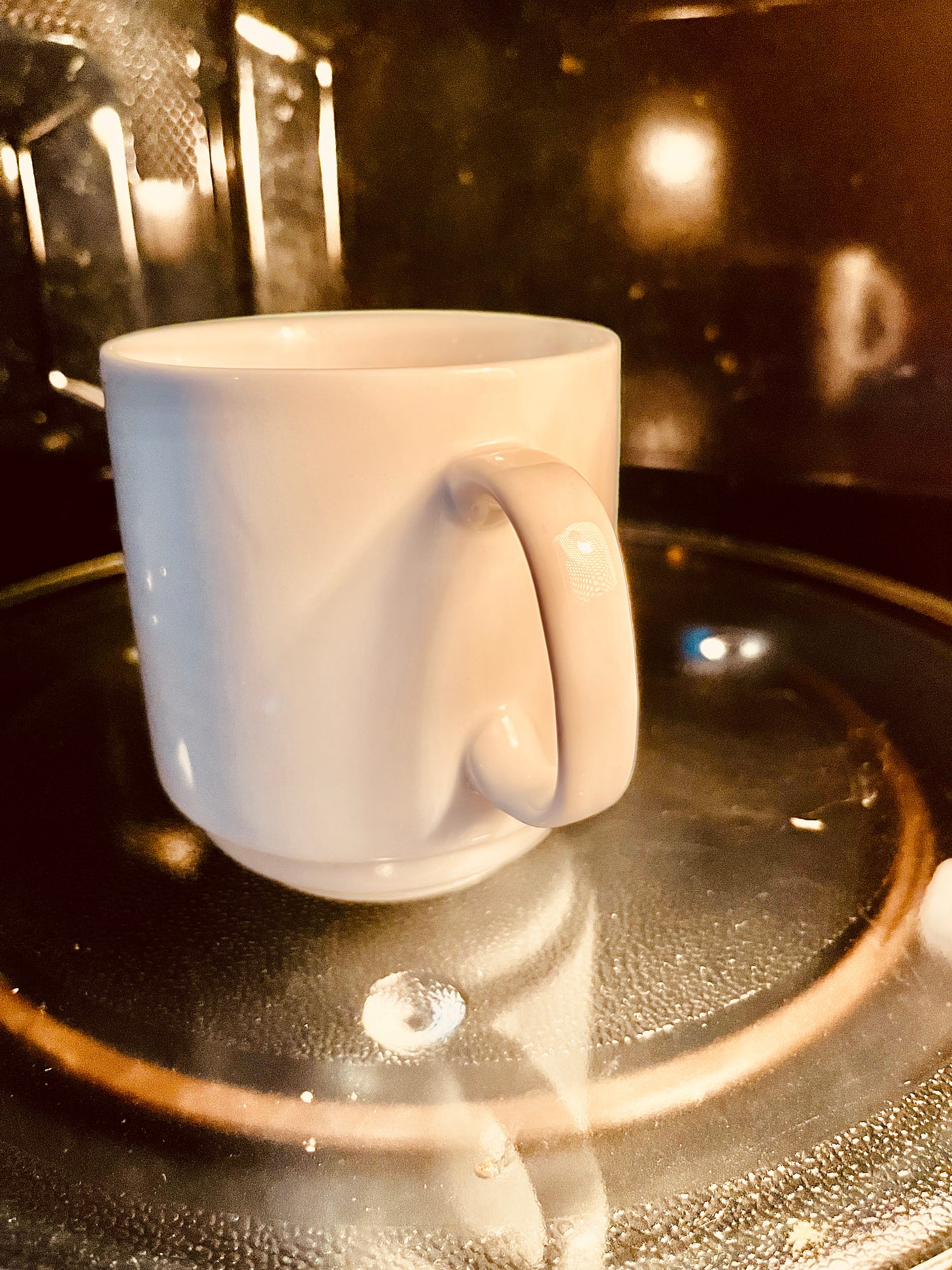 White cup of coffee in a microwave oven. Photo taken by poet/author, Tess McCarthy. 