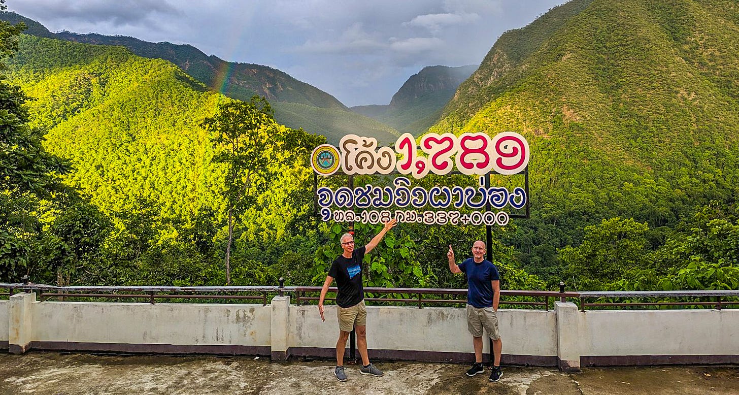 Brent and Michael standing next to an overlook, jungle-covered mountains behind us as we gesture at the sign. 