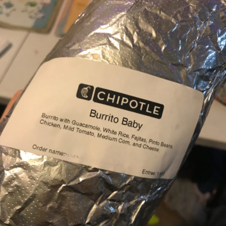 A photograph of a foil-wrapped burrito with a white label. The label has the Chipotle logo on top and says "Burrito Baby" where the order name goes. Under that is the order: Burrito with Guacamole, White Rice, Fajitas, Pinto Beans, Chicken, Mild Tomato, Medium Corn, and Cheese.