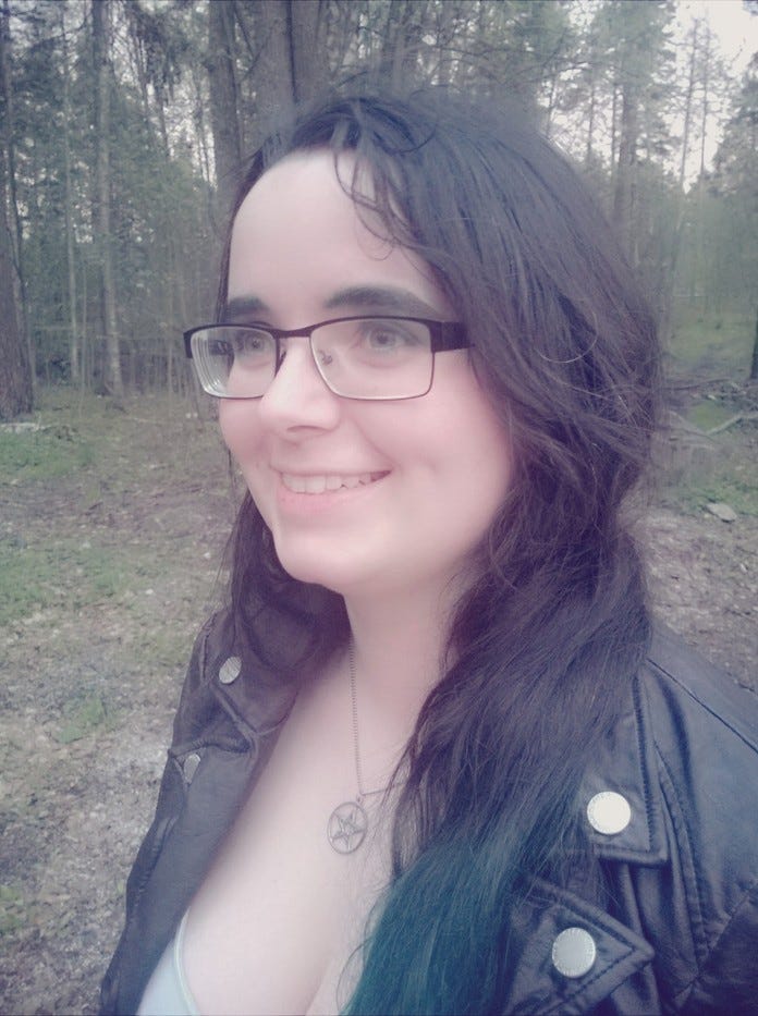 Picture of Sia Tukiainen. She is wearing a leather jacket and walking through a forest.