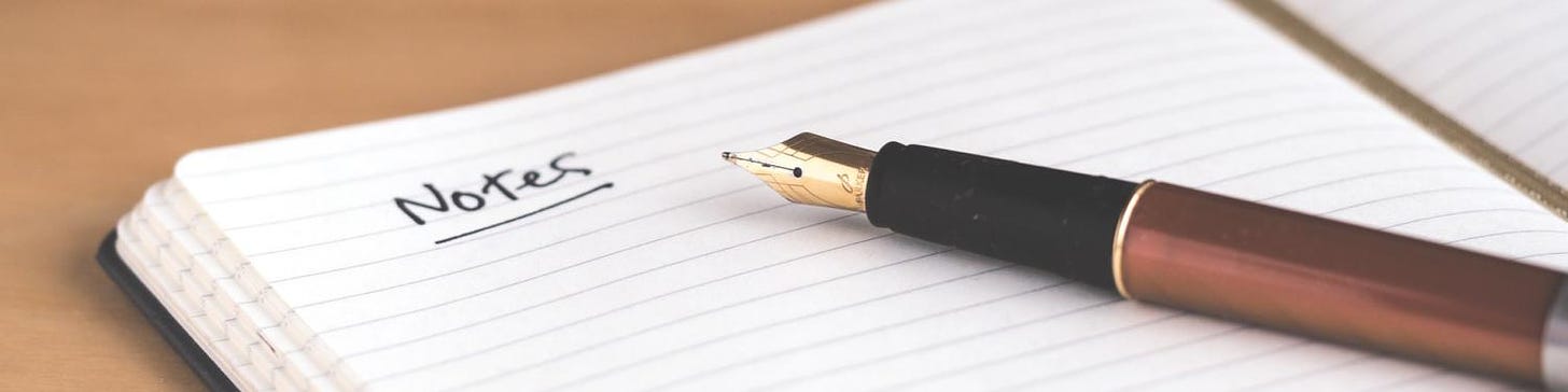 A pen laying on an open notebook with the word "note" written on the page. 