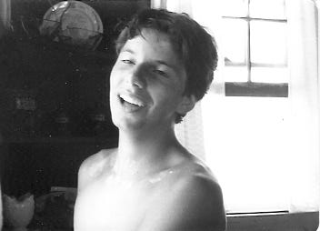 Black & white snapshot of a shirtless boy in a kitchen