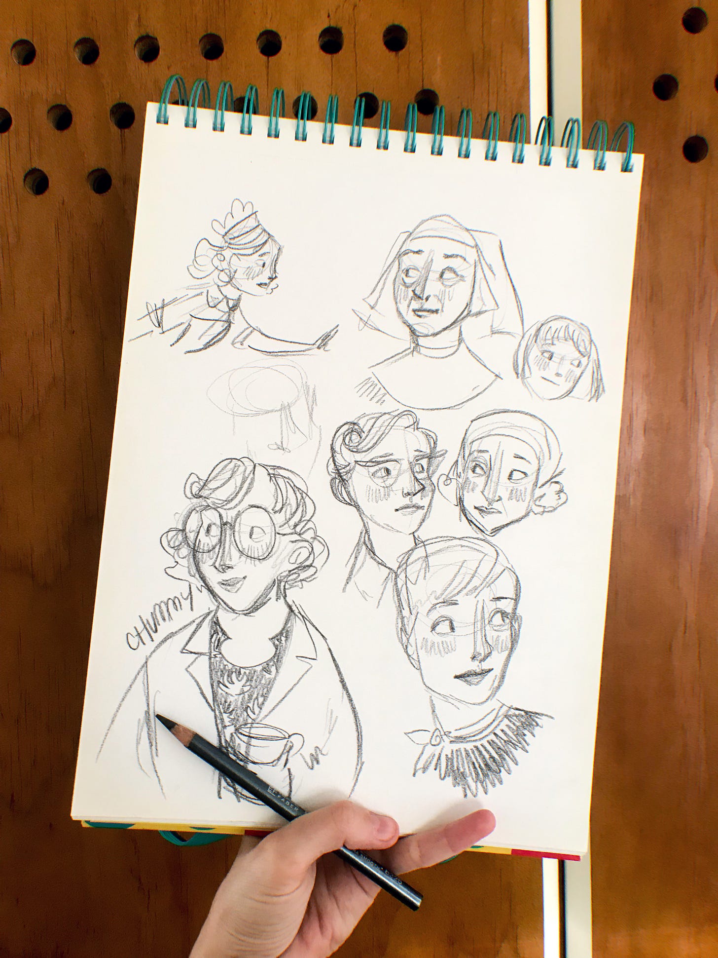 A photo of Gracie's hand holding up a sketchbook, with various sketches of Call the Midwife tv show characters on it