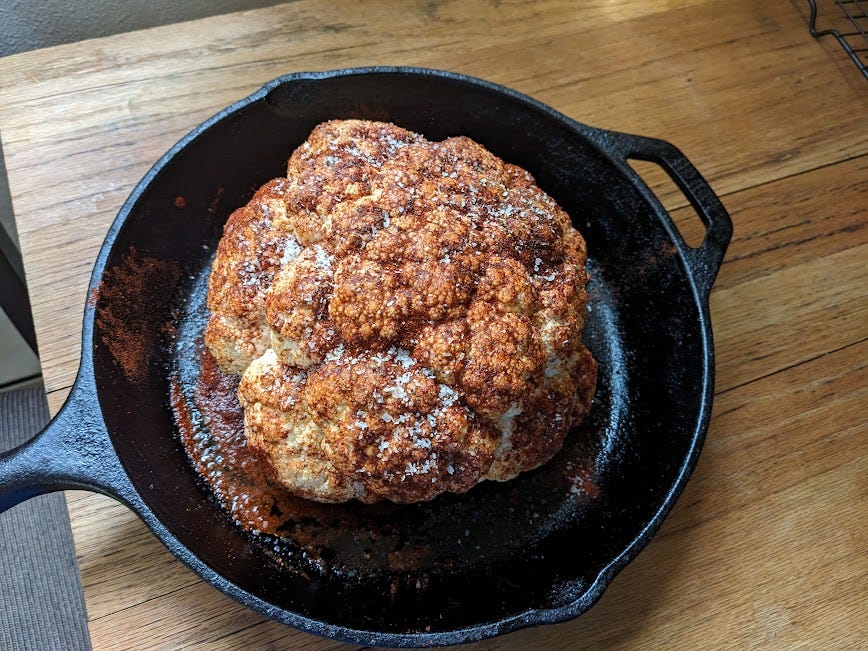a big cauliflower sits in a cast iron, rubbed with spices