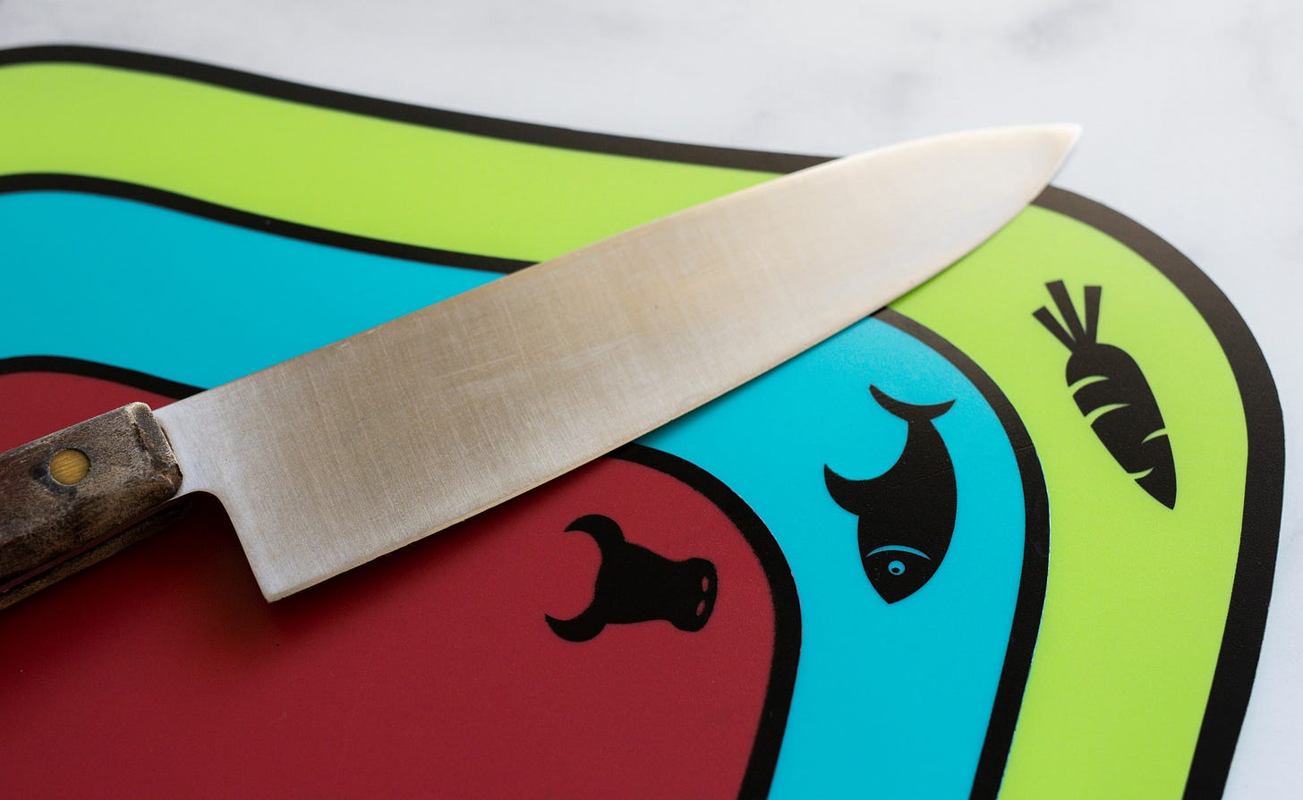 A knife laying on top of three cutting boards. Each cutting board is a different color which corresponds with a food icon to help prevent cross contamination.