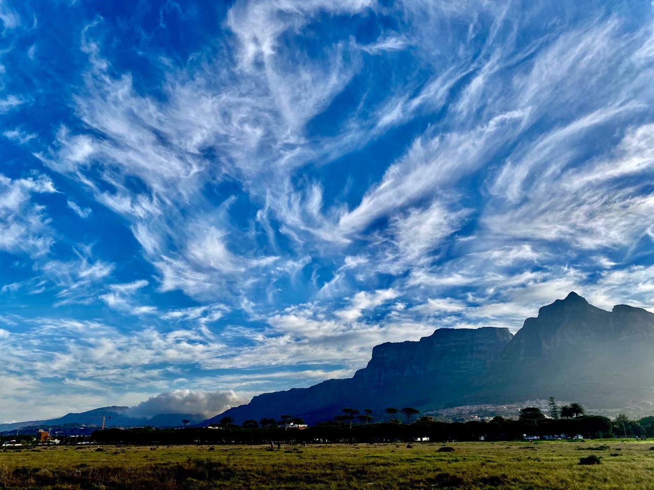 a landscape view of a mountain with whispy white clouds against a cornflower blue sky