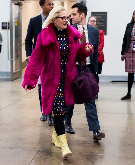 A person in a pink coat and yellow boots walking in a hallway

Description automatically generated