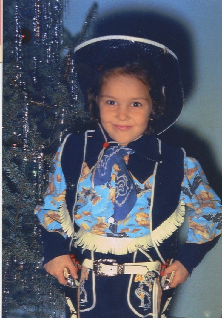 Six year old Jo, eyes ablaze with joy, in her brandnew cowboy suit with a two-gun holster.