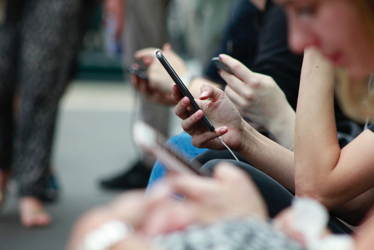 A soft focus image of hands holding smartphones, with people staring at their screens