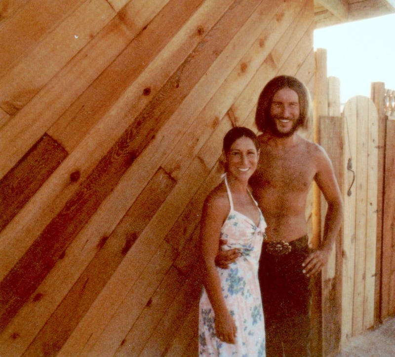 Photo of cabin owners by Sherry KIllam Arts showing woodwork on outside of 80's cabin.
