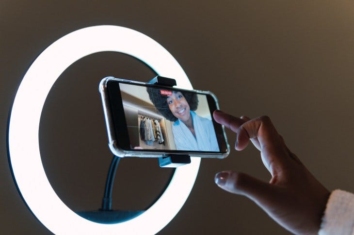 Smiling woman vlogging on smart phone in illuminated ring light at home