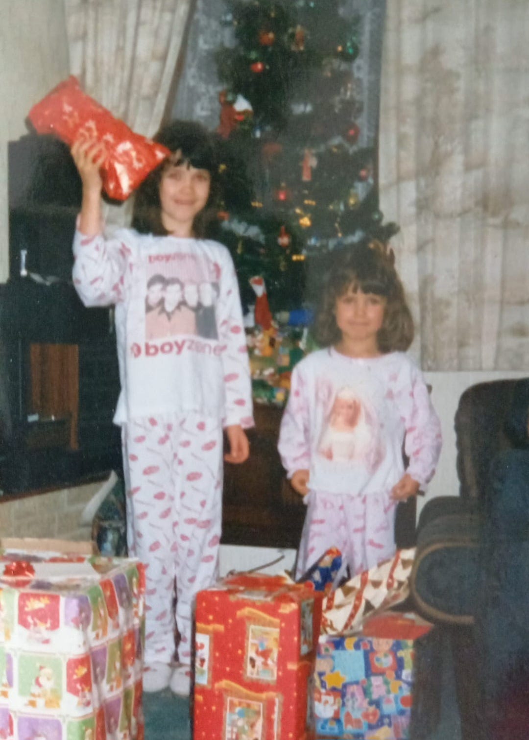 My sister and I as children standing with our Christmas presents in front of the tree in the late 90s.  We both have brown hair and fringes. I'm wearing Boyzone PJs, Leanne is wearing Barbie PJs