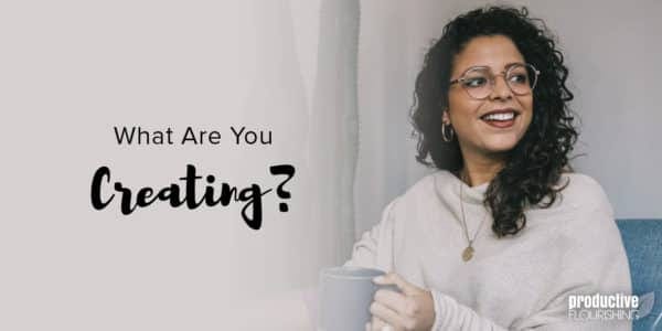 A woman wearing glasses with dark, curly  hair sits on a couch with a mug, smiling, looking to the right side of the frame. Text Overlay: What Are You Creating?