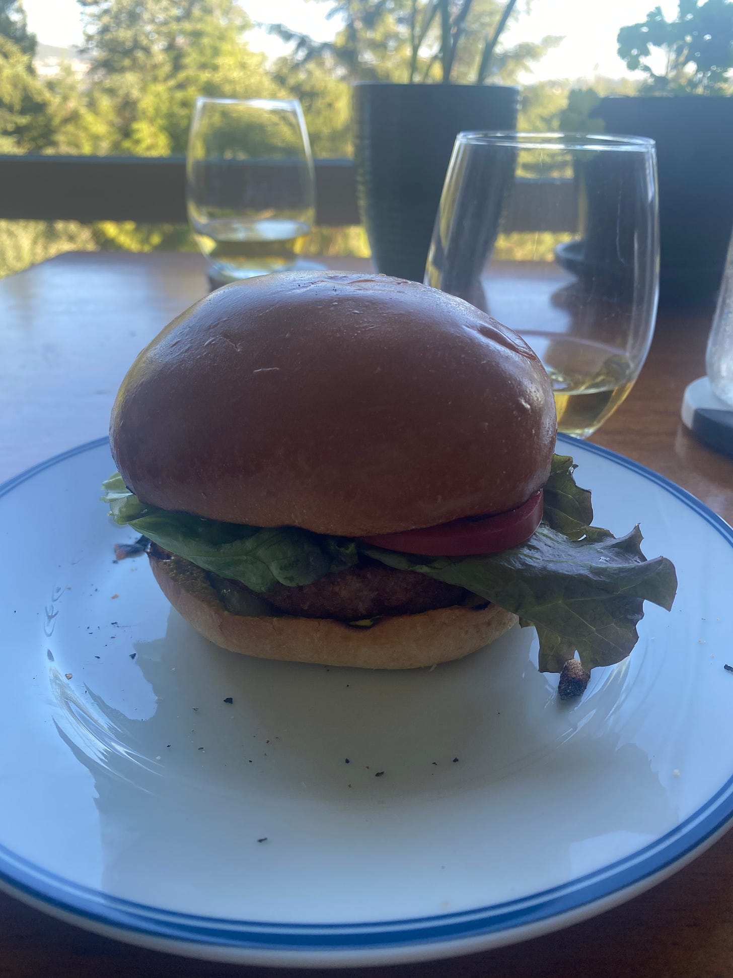 A veggie burger on a white plate with a blue rim. There's a glass of white wine in the background.