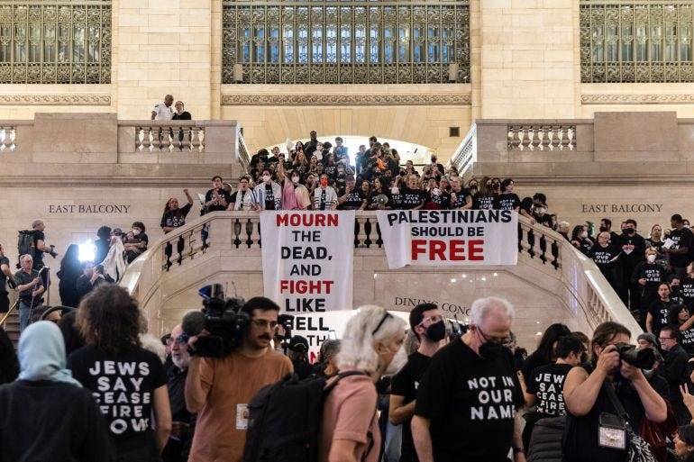 Protesters gathered on the concourse of New York's Grand Central Station. They are wearing black and hanging a banner reading 'Palestinians must be free' from the top of the staircase