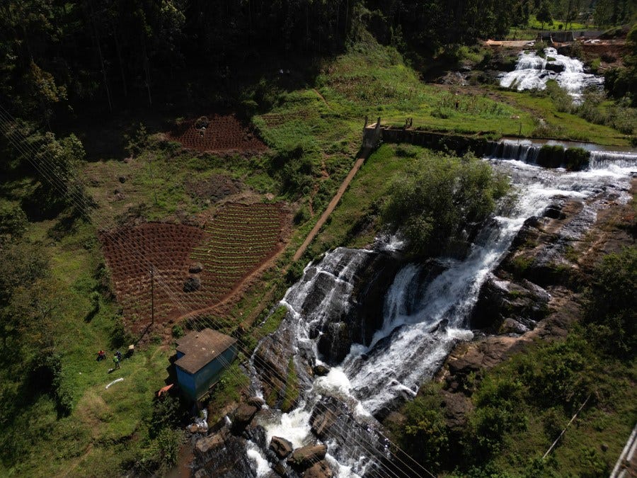 A small dam above a steep waterfall, surrounded by steep green fields, in rural Africa