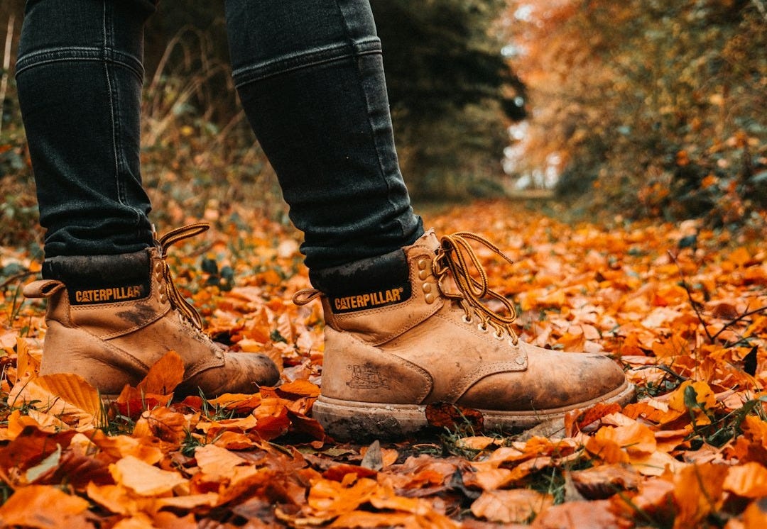 man wearing brown Caterpillar leather work boots standing on ground with leaves