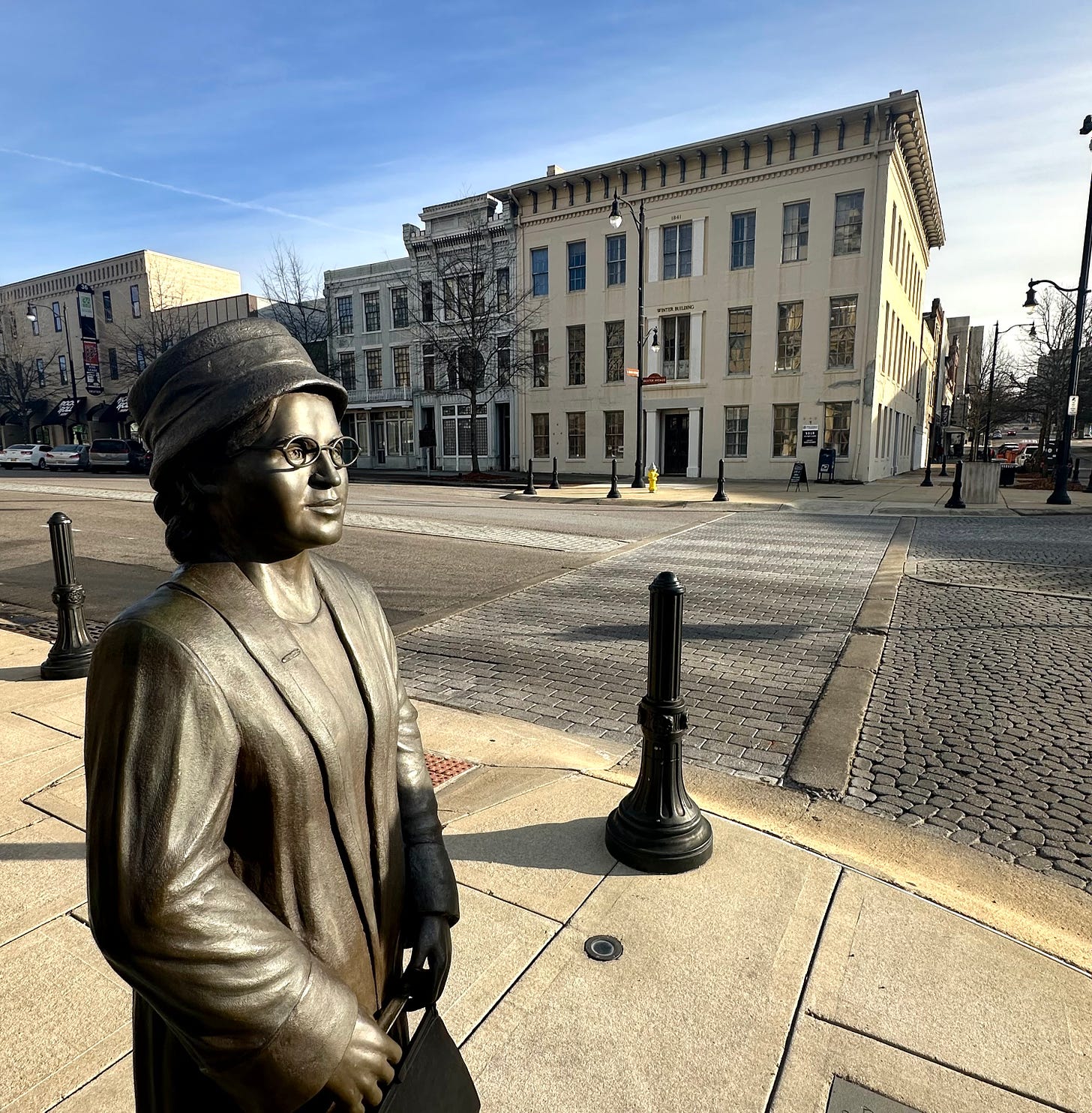 Rosa Parks statue on Dexter Avenue facing the Court Square Fountain, with the Winter Building in the background. Author photograph. February 1, 2024.Rosa Parks statue on Dexter Avenue facing the Court Square Fountain, with the Winter Building in the background