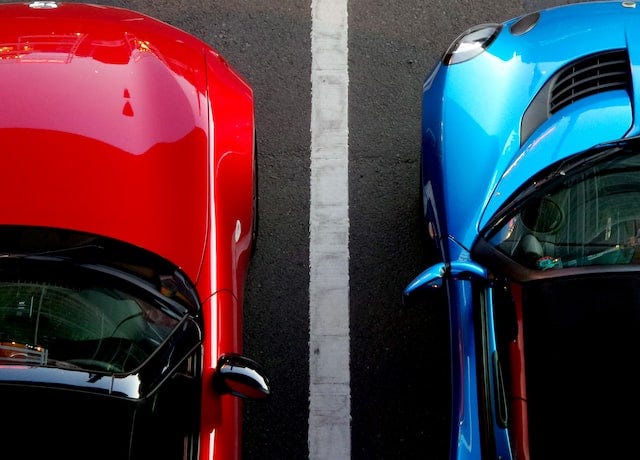 photo from above of two cars on either side of a parking lot line. One car is shiny red and then other is shiny blue