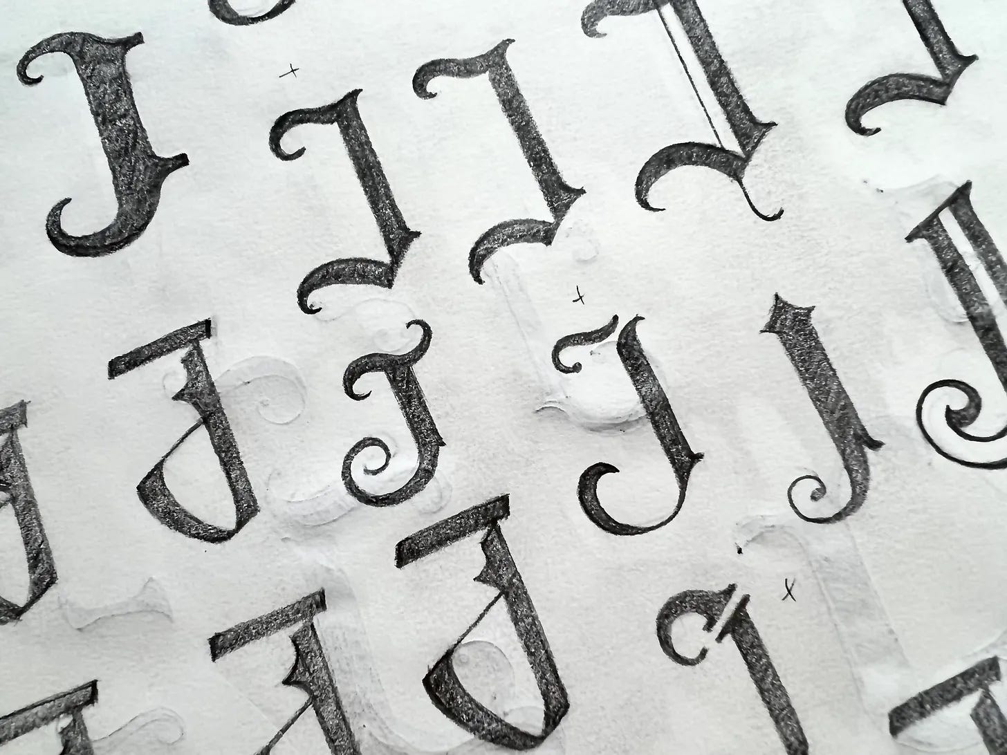 A photograph of a page filled with a variety of hand-drawn iterations of the Jaques logo, all variations of the letter J in a Gothic font.