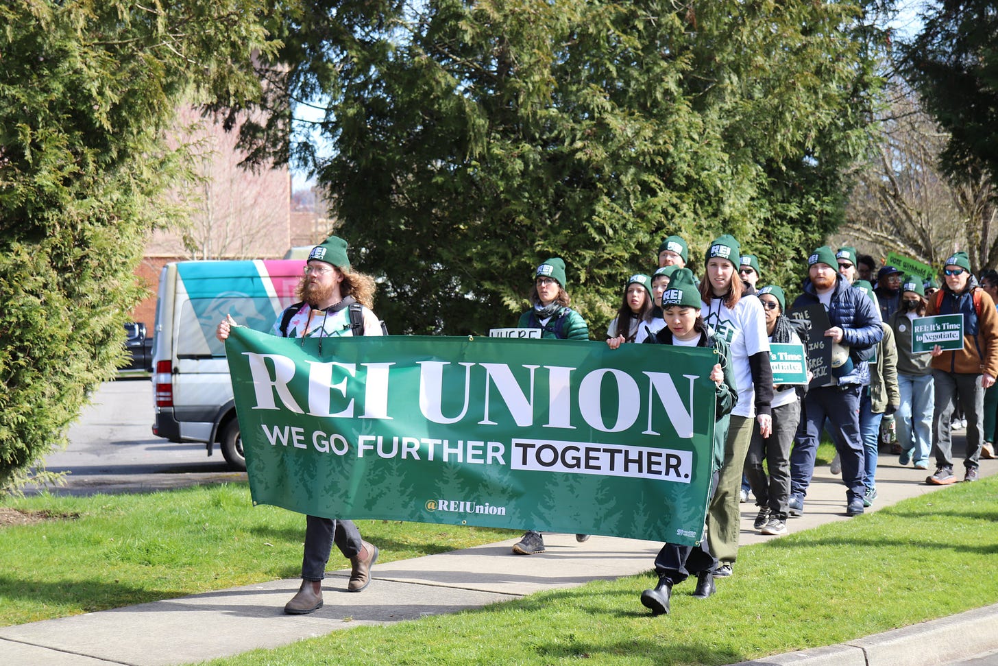 REI Union workers from across the country led the march to REI Headquarters in Issaquah Washington. At the front of the march workers display their union banner, "REI UNION, We Go Further TOGETHER."