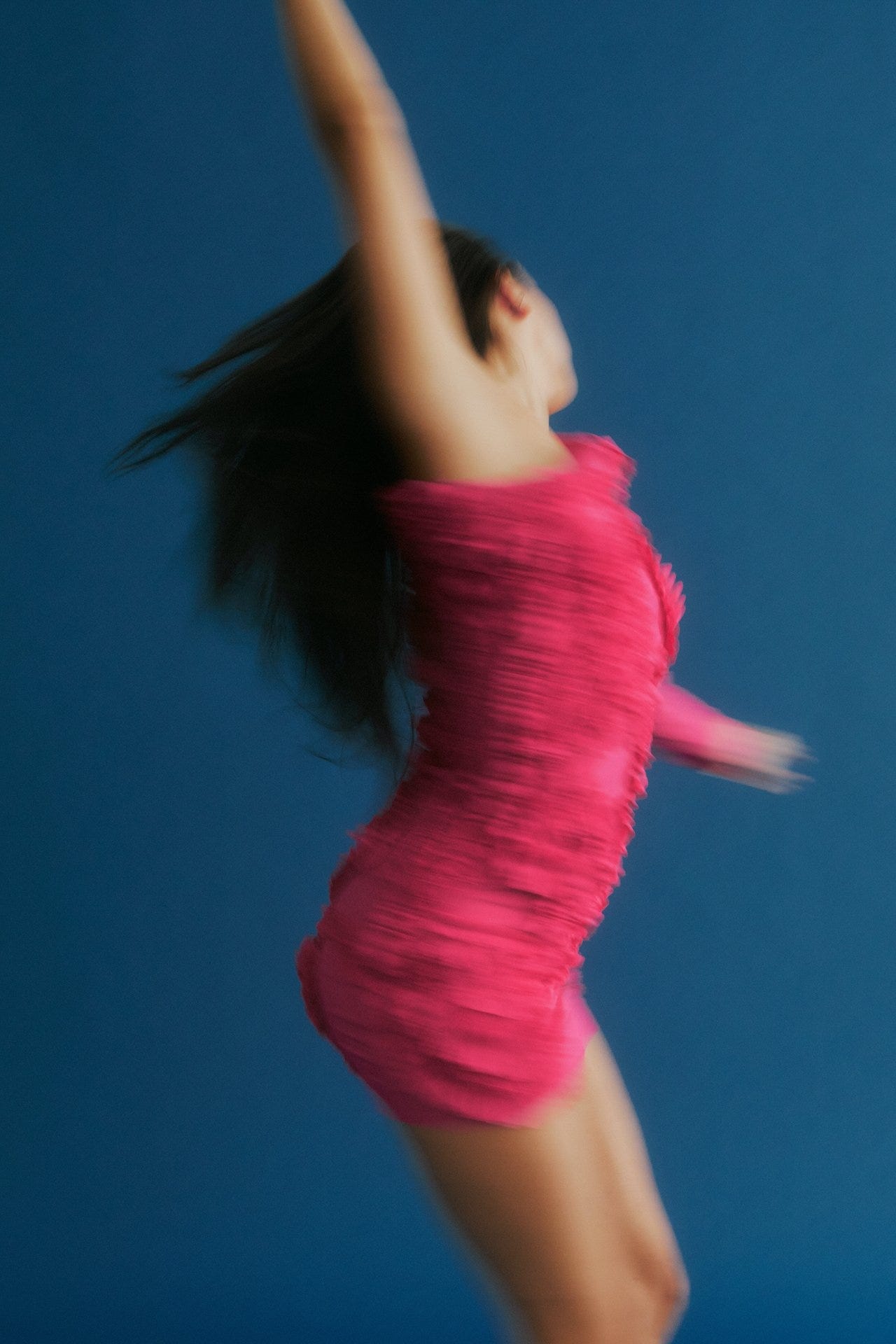 A woman dressed in hot pink dances in a blur in front of a denim blue wall
