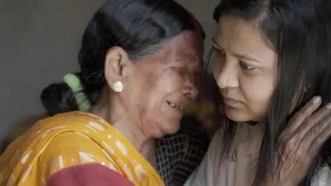 BBC Siro, an elderly midwife wearing a yellow sari, sobs as she clings on to Monica - a woman with long dark hair in her late 20s