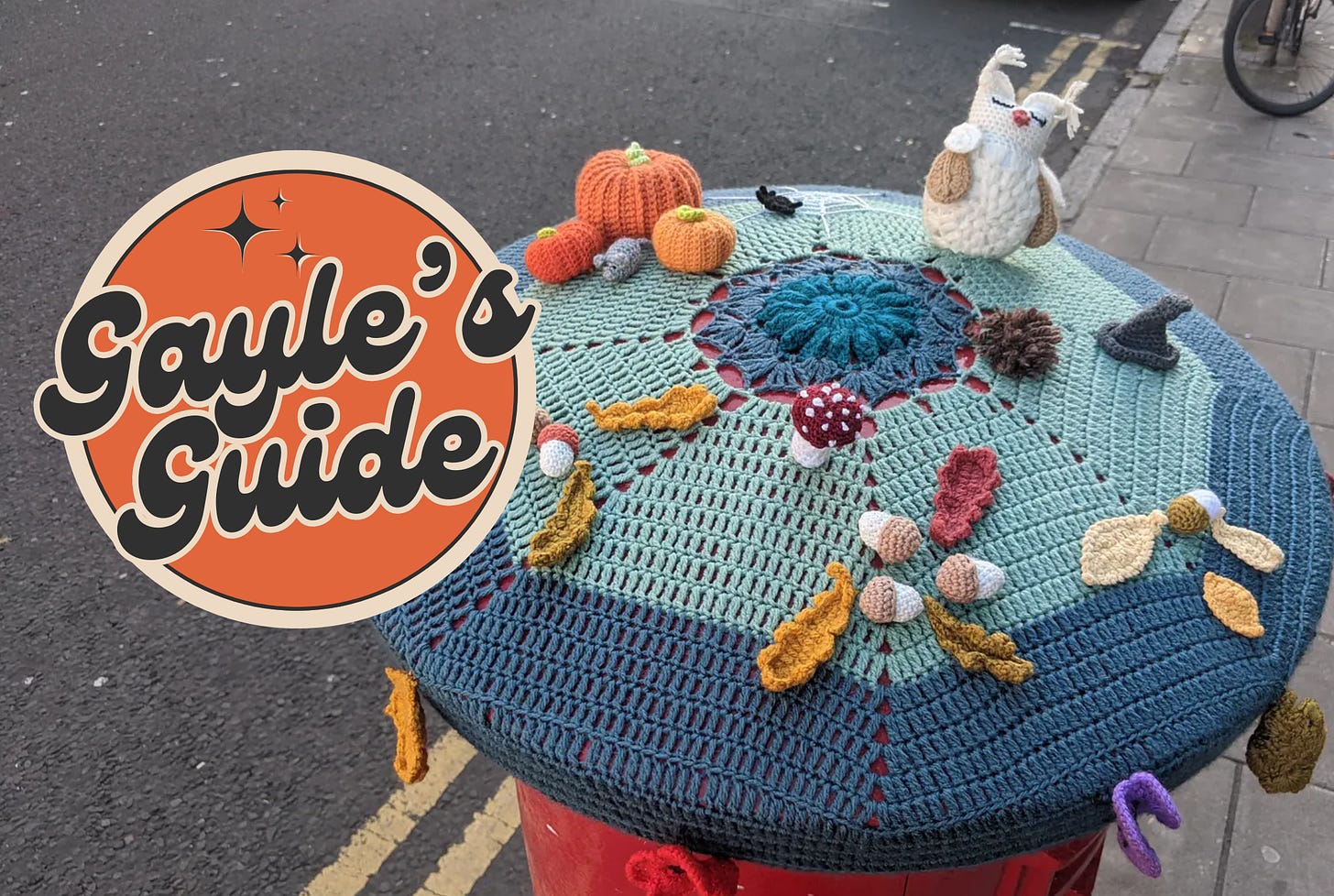 Crochet cover on a post box with pumpkins, mushrooms, acorns, leaves and an owl on top. Gayle's Guide logo