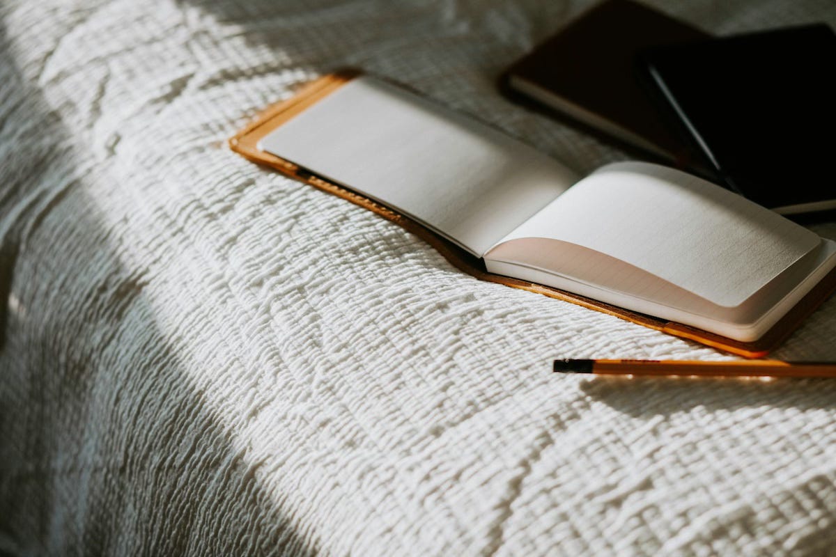 A notebook and pen on a bed.