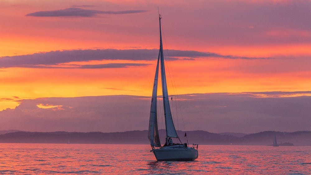 A sailboat underway with a beautifully colored late-day sky in the background.