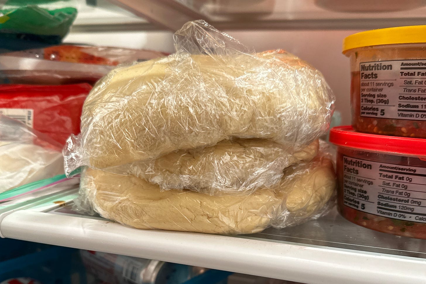 cookie dough wrapped in plastic wrap on a fridge shelf