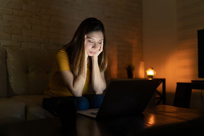A sad-looking woman sitting at a laptop in the dark. A sad-looking woman sitting at a laptop in the dark.