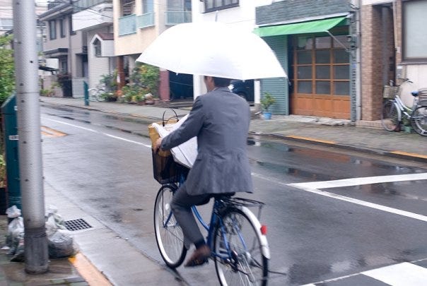person riding a bicycle in the rain, holding an umbrella, and reading a newspaper while wearing a business suit - Laurie McGinley 2009