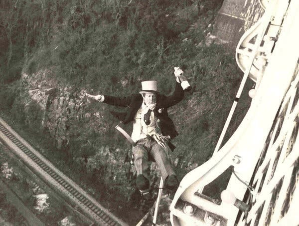 A black-and-white photo of David Kirke in mid-plunge from a bridge, his body facing upward. He is wearing a suit and a top hat and holding a bottle of Champagne in his left hand.