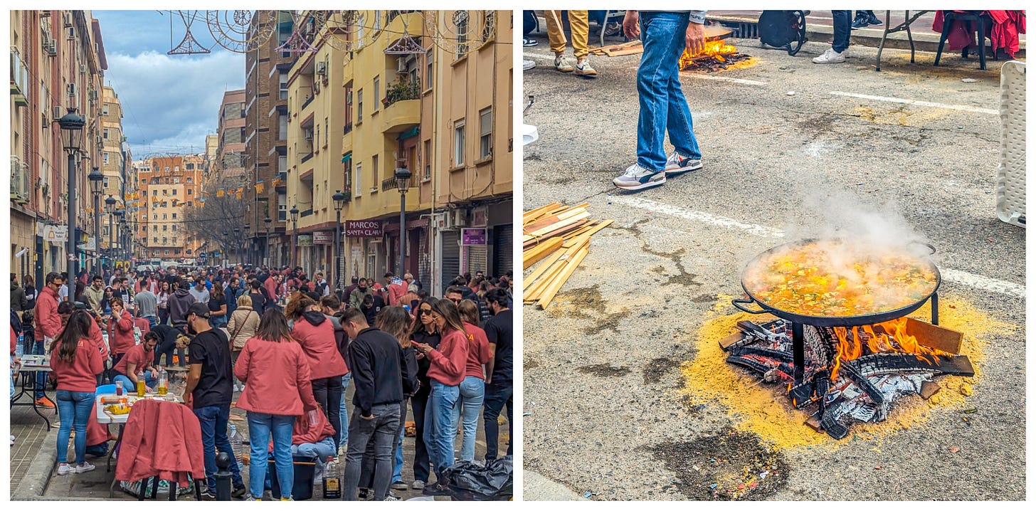 On the right, Valencians gathered on the street, on the right a big pan of paella cooking on the street. 