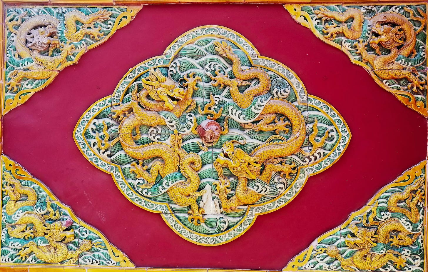 Fotografia em cores de detalhe da decoração em templo no Beihai Park, mostrando dois dragões dourados ao redor de uma pedra vermelha.