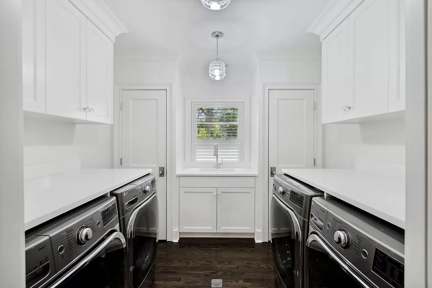 A bright white laundry room with two sets of front loading washer/dryers.