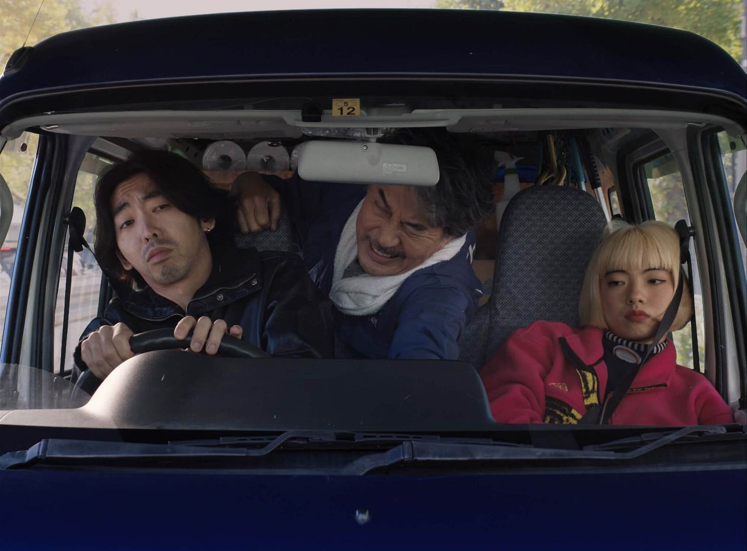 A shot through a van's windscreen of (from left to right) Takashi (Tokio Emoto) in the driver's seat, Hirayama (Kōji Yakusho) in the back seat and Aya (Aoi Yamada) in the passenger seat