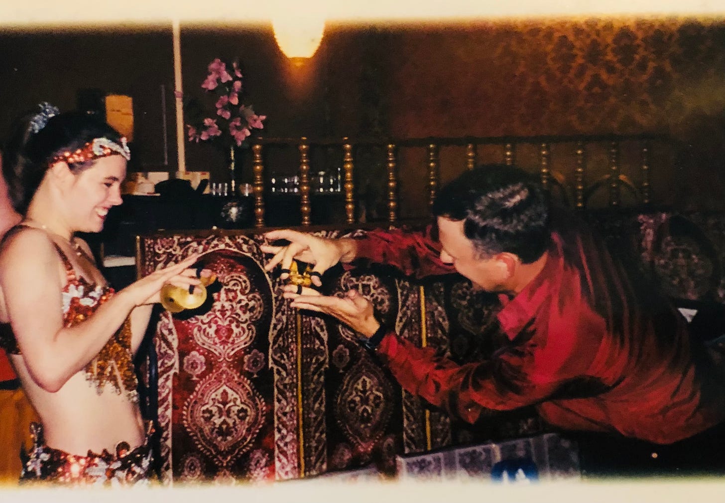 The author in a spangly copper costume playing finger cymbals with a patron in an ornate Moroccan restaurant.