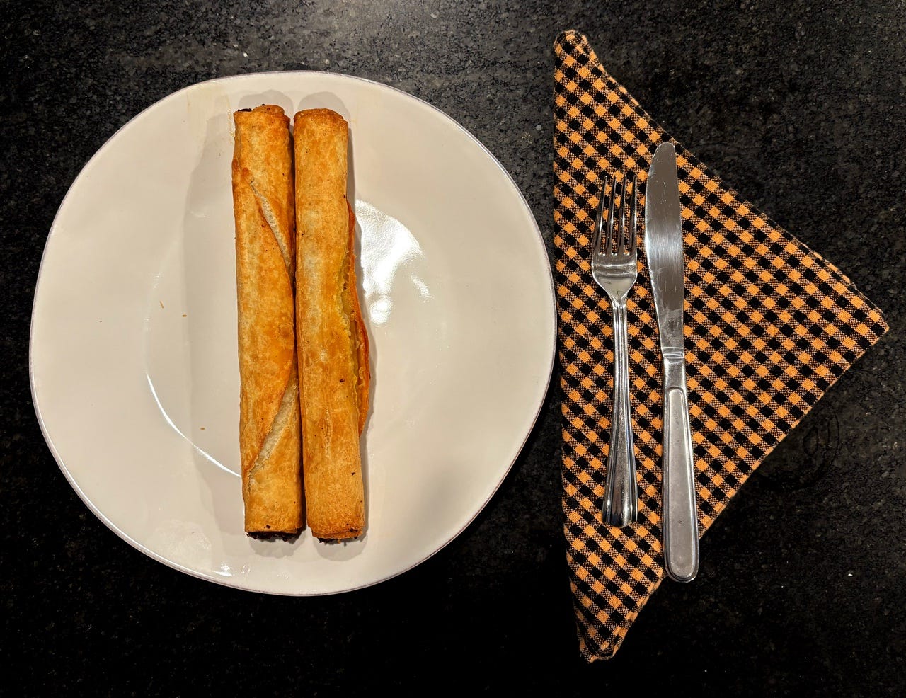 Two burritos on a plate, with a knife, fork, and napkin.