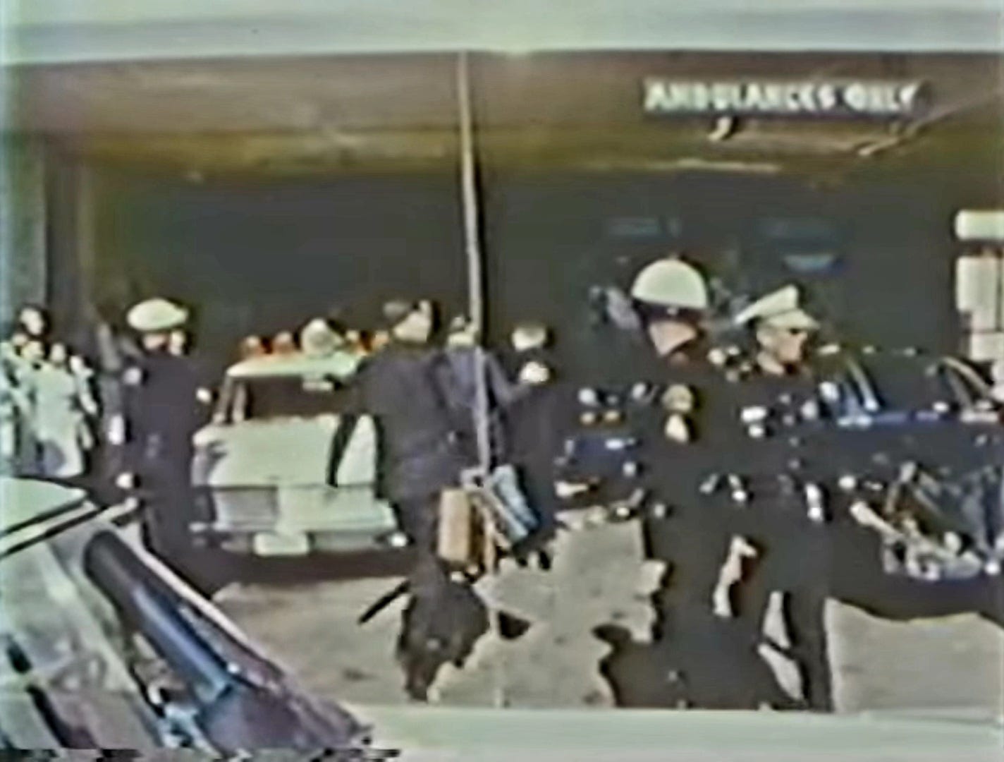 Atkins film frame showing Dr. Burkley (center, black suit) entering Parkland past the limousine (right) with rear top on the car.