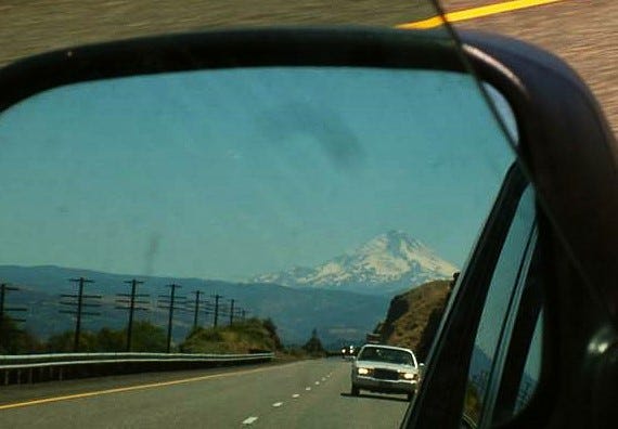 a photo of a mountain in the rearview mirror on the driver's side of a car