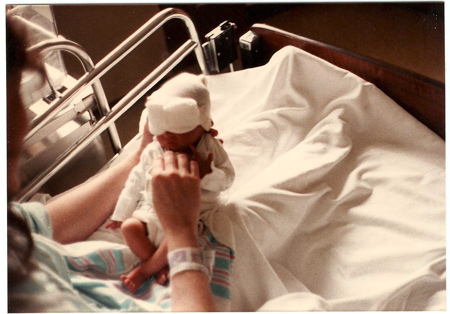 In a hospital bed a mother holds a tiny baby. His eyes are covered with thick gauze to keep the light out. 