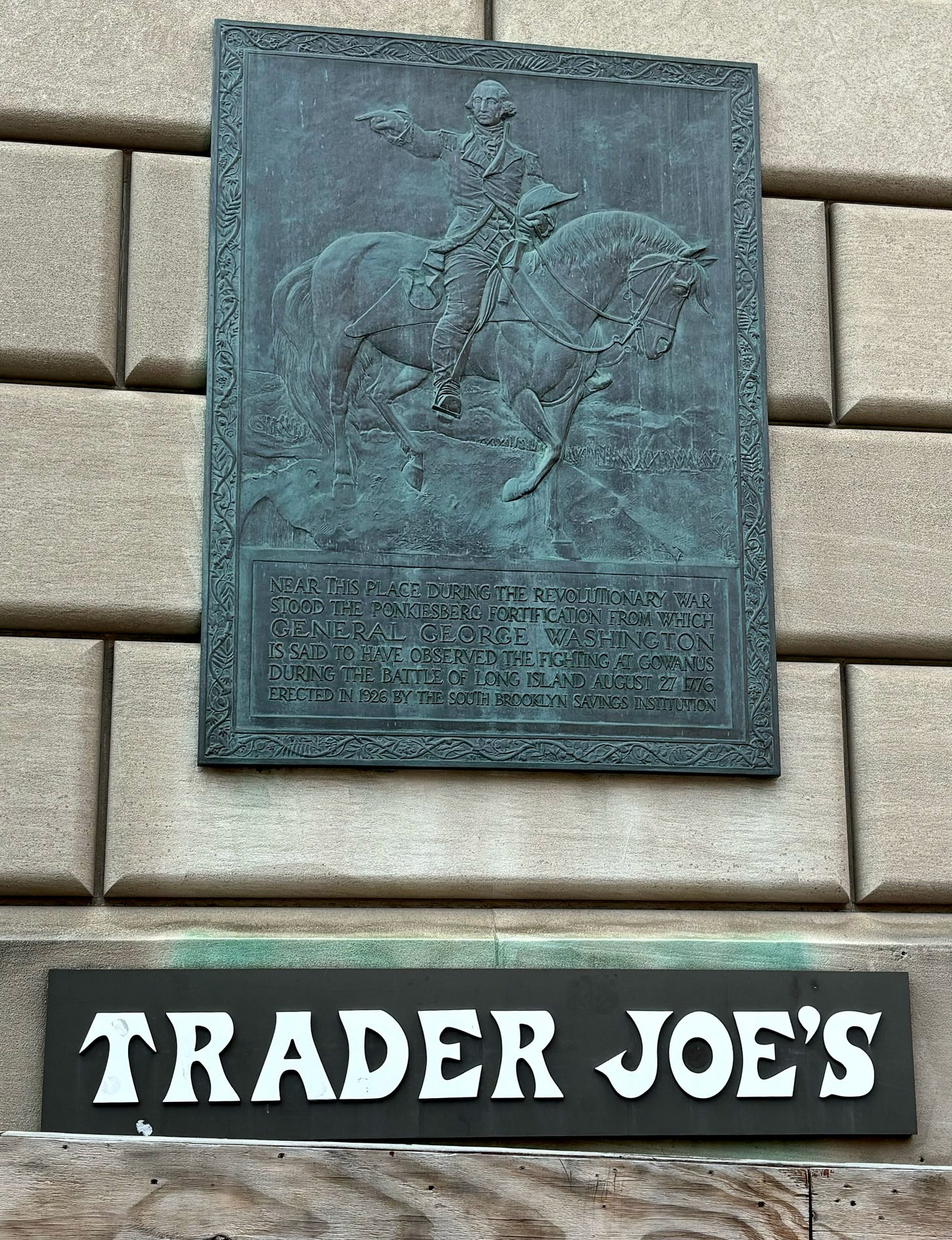 A metal plaque framed in ornate ivy. It is dominated by a relief of Washington on his horse, pointing out to his right. It reads: Near this place during the Revolutionary War stood the Ponkiesberg fortification from which General George Washington is said to have observed the fighting at Gowanus during the Battle of Long Island August 27, 1776. Erected in 1926 by the South Brooklyn Savings Institution.